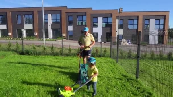 O pequeno filho corta relva com cortador de brinquedos, tal como o pai. Gimbal mover frente — Vídeo de Stock