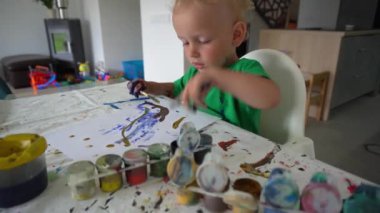 Çocuk, fırça ve kağıt üzerinde parmak kullanarak büyük bir hevesle bıyıkla resim yapıyor.