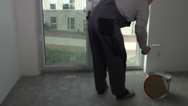 Работник берёт белую краску из ведра со стороны роллера и окна краски — стоковое видео