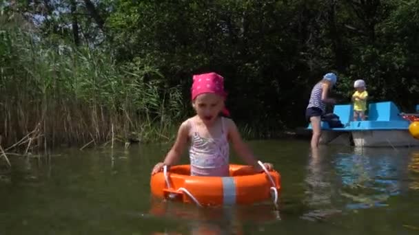 Leuk meisje waden in het water met badpak en reddingsboei. Moeder met kleine jongen — Stockvideo