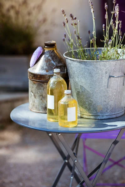 Um balde com flores de lavanda fica em uma mesa com garrafas de óleo de lavanda — Fotografia de Stock