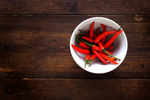 Bowl of chili peppers on textured wood background