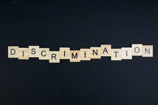 Discriminação- palavra composta de blocos de madeira letras sobre fundo preto, espaço de cópia para texto do anúncio . — Fotografia de Stock
