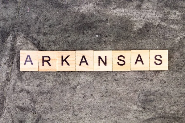 Arkansas ord skrivet på träblock, på grå betong bakgrund. Ovanifrån. — Stockfoto