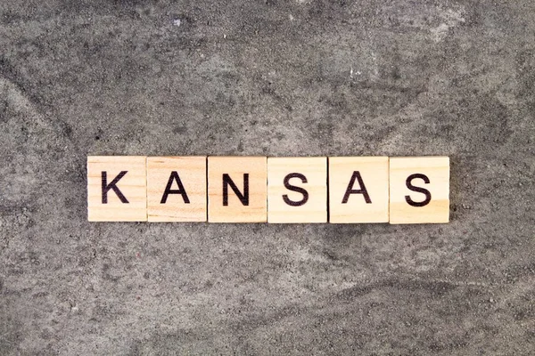 Kansas woord geschreven op houten blok, op grijze betonnen achtergrond. Bovenaanzicht. — Stockfoto