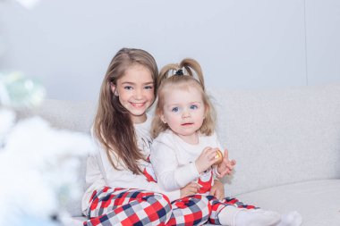 Noel ağacının yanında iki kız kardeş. Şirin küçük kızlar. Ev rahatlığı. Noel süslemesi.