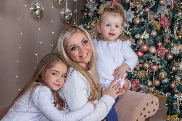 Mom and daughters at the Christmas tree. Christmas season. Sisters. Merry Christmas and happy holidays Cheerful mom and her cute daughters exchange gifts.