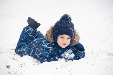 little boy lying in snow while playing in winter park