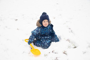 little boy lying in snow while playing in winter park