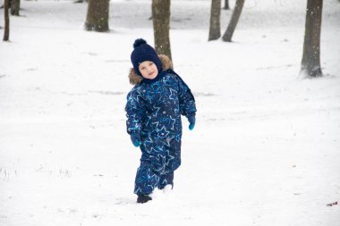 Küçük çocuk kışın parkta yürüyüşe çıktı. Kış Parkı. Kış tulumlu bir çocuk. Parkta kar .