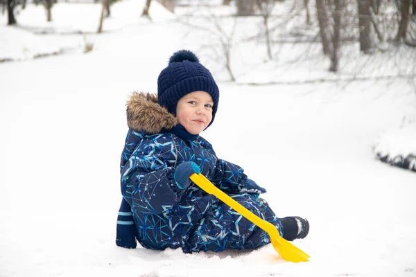 Petit garçon en promenade dans le parc en hiver. Parc d'hiver. Un garçon en salopette d'hiver. Neige dans le parc  . — Photo