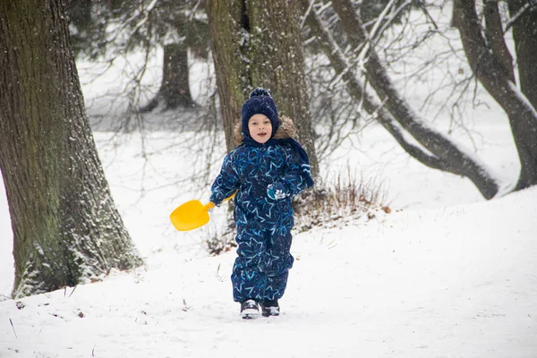 Petit garçon en promenade dans le parc en hiver. Parc d'hiver. Un garçon en salopette d'hiver. Neige dans le parc  . — Photo