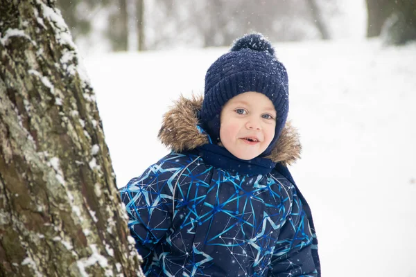 Petit garçon en promenade dans le parc en hiver. Parc d'hiver. Un garçon en salopette d'hiver. Neige dans le parc  . — Photo