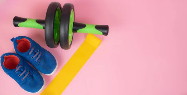 Sports yellow elastic band . Sports equipment. Yellow elastic band on a pink background. Green dumbbell. Sports sneakers. Training shoes.