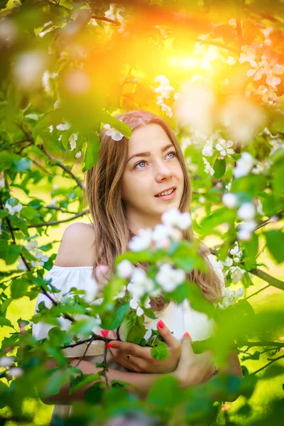 Retrato de una niña en un manzano floreciente. Una hermosa chica mira en el marco. Sonríe. Chica de pelo rubio. El árbol floreciente. Retrato — Foto de Stock