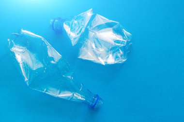 Katı mavi arka planda plastik şişe. Çevreyi koru. İkincil hammadde. Çöp işleme. Doğayı koru. Plastiğin tehlikeleri hakkında makale. Çevre hakkında makale