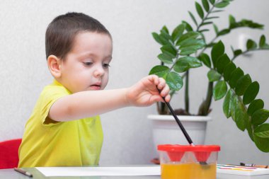 Çocuk boyalarla resim çiziyor. Evinde otur. Uzaktan eğitim. Çocuklar için eğitim dersleri. Çocukların boş vakitleri hakkında bir makale. Evde çocuk dersleri. Resimler