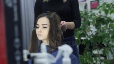Kadın kuaför ayakta ve güzellik salonundaki güzel genç bayana saç stili yapıyor.