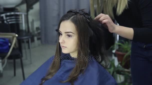 Vrouwelijke kapper staande en het maken van kapsel tot schattige mooie jonge vrouw in schoonheidssalon — Stockvideo