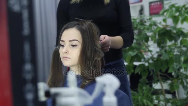 Peluquería femenina de pie y haciendo peinado a linda joven encantadora en el salón de belleza — Vídeo de stock