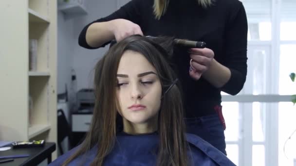 Peluquería femenina de pie y haciendo peinado a linda joven encantadora en el salón de belleza — Vídeos de Stock