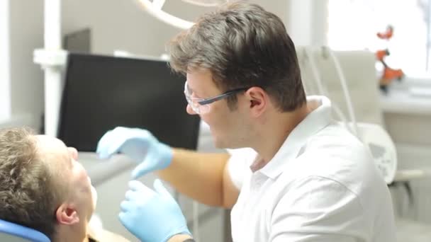 Der Hauptzahnarzt kommuniziert mit dem Patienten und führt eine Untersuchung der Mundhöhle durch — Stockvideo