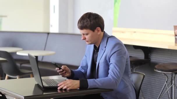 Mladý podnikatel pracuje na počítači a s telefonem v kavárně — Stock video