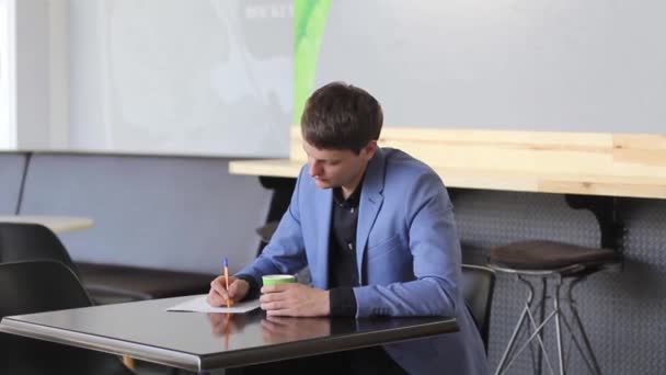Молодой предприниматель пишет бизнес-план в кафе — стоковое видео