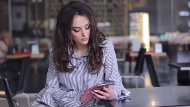 Beautiful young woman while in the cafe uses her mobile device — Stock Video