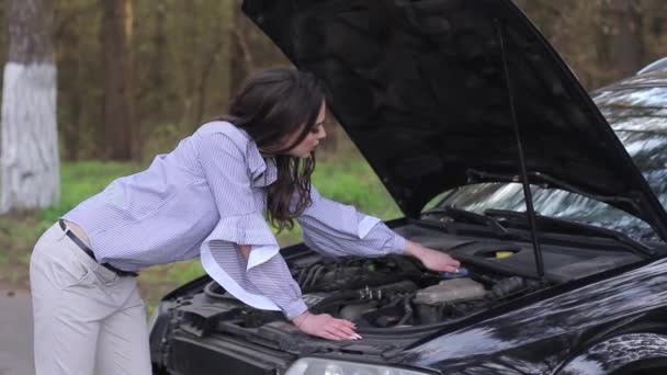 Attraktiv ung kvinna titta under huven på bilen — Stockvideo