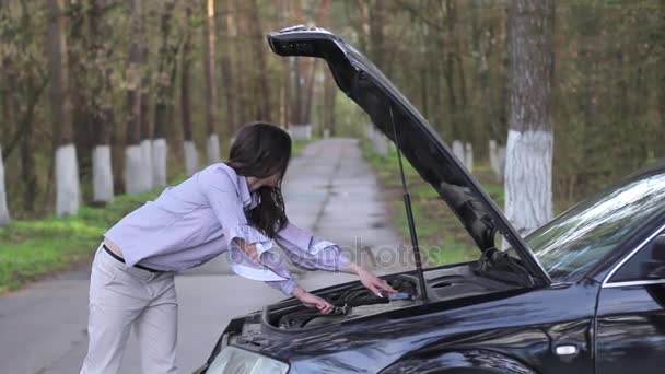 Mujer inclinada sobre el compartimiento del motor de un coche averiado — Vídeo de stock