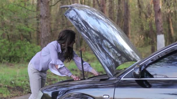 Mujer inclinada sobre el compartimiento del motor de un coche averiado — Vídeo de stock