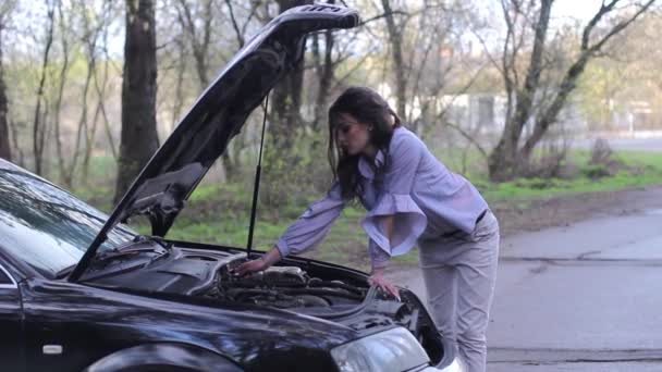 Atractiva mujer joven que mira debajo de la capucha del coche — Vídeo de stock