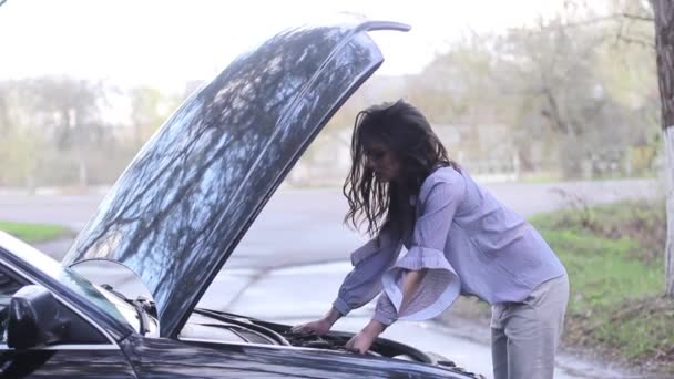 Jonge vrouw ziet er onder de motorkap van zijn auto, die brak — Stockvideo