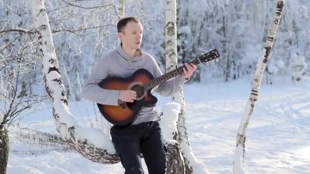 雪に覆われた森の中ギターを弾く若い男 — ストック動画