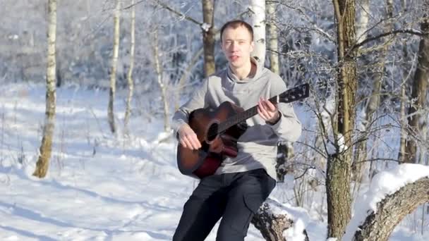 Молодой парень играет на гитаре в заснеженном лесу — стоковое видео