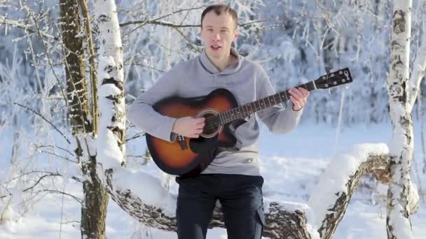 Молодой парень зимой играет на гитаре — стоковое видео