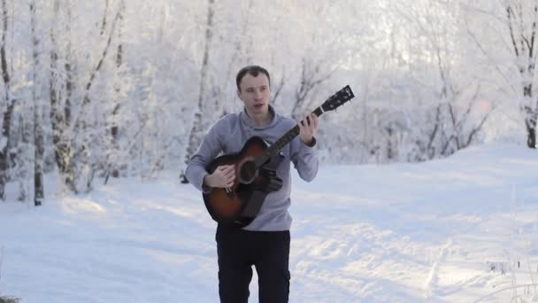 Junger Mann spielt Gitarre im verschneiten Wald — Stockvideo