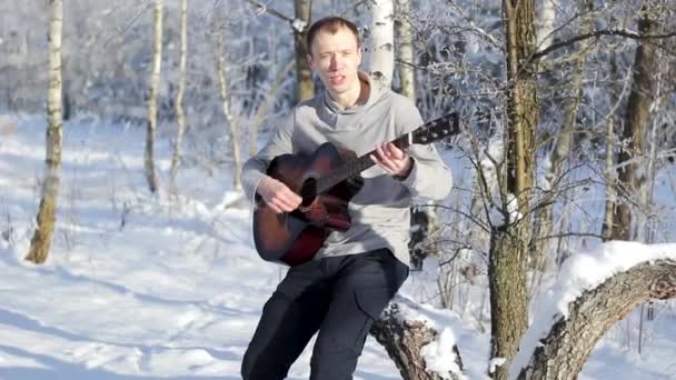 Junger Mann spielt Gitarre im verschneiten Wald — Stockvideo