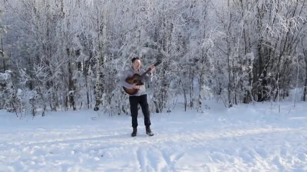 Młody chłopak gra na gitarze w zaśnieżony Las — Wideo stockowe