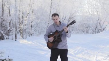 genç adam karlı ormandaki gitar çalmak