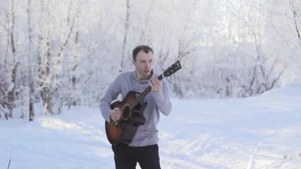 Genç adam karlı ormandaki gitar çalmak — Stok video