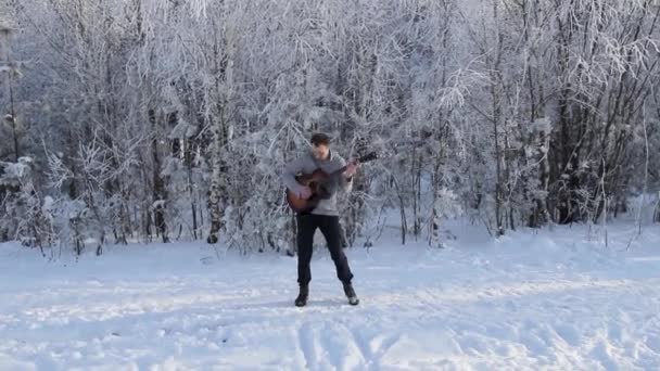 Молодой парень играет на гитаре в заснеженном лесу — стоковое видео