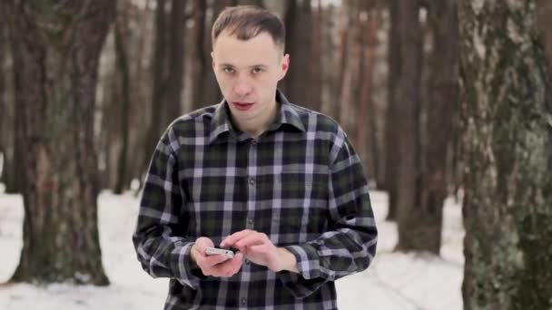 Tipo en el bosque frío cubierto de nieve con un teléfono móvil — Vídeos de Stock