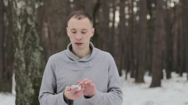 Хлопець у засніженому холодному лісі з мобільним телефоном — стокове відео