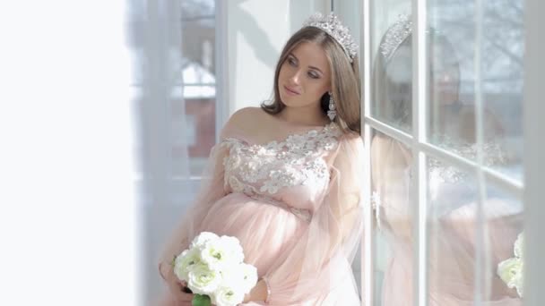 Pregnant girl sits near a window in a beautiful pink dress — Stock Video