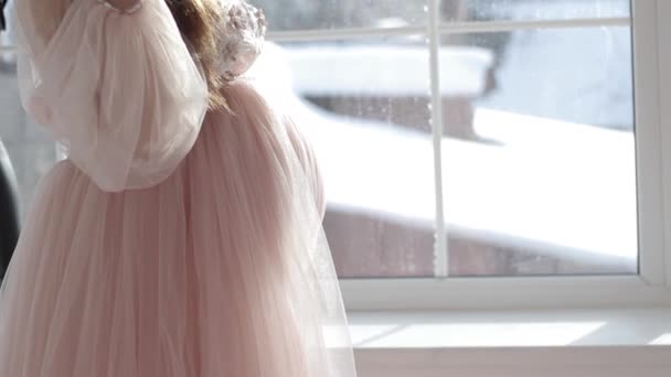 Dziewczyna w ciąży siedzi w pobliżu okna w pięknej różowej sukience — Wideo stockowe