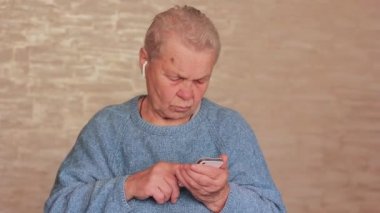 Kulaklık takan, telefonla dans eden ve eğlenen yaşlı bir kadın. Kulaklıklı büyükanne.