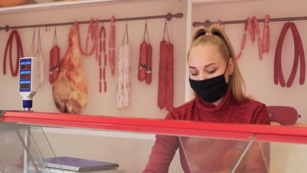 Een verkoper met een medisch masker verkoopt worst vanwege een coronovirus. Coronovirus, verkoper in het departement worst en kaas. — Stockvideo