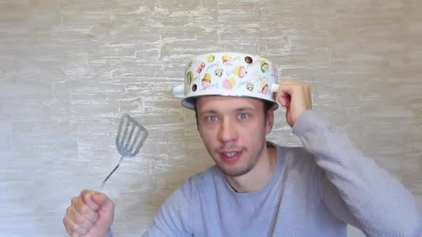 Un fou avec une casserole sur la tête et un objet de cuisine dans les mains . — Video